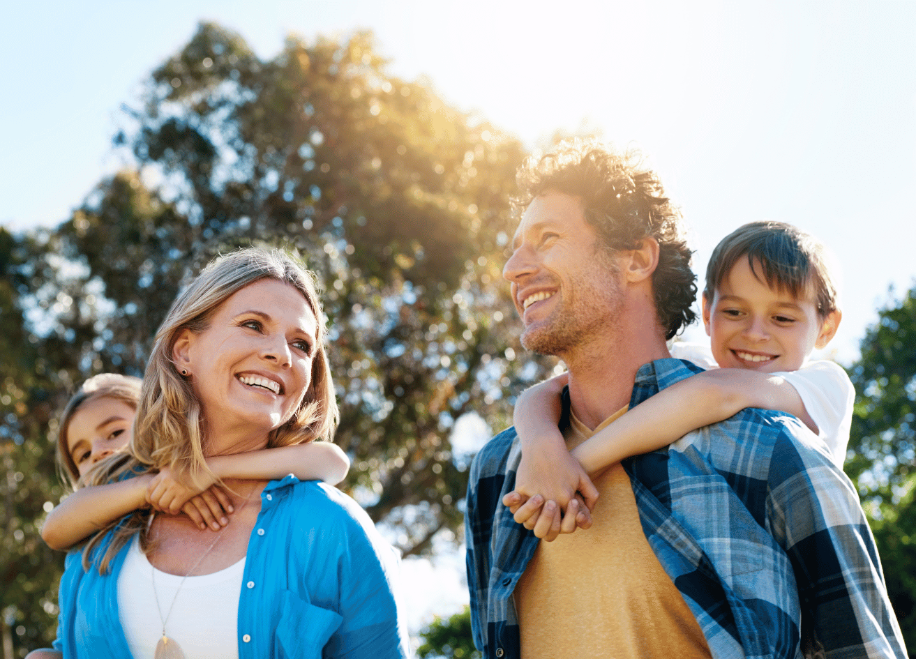 Family play in the sunshine outside. Woman with blonde hair carries little gift, and man with brown hair carries little boy